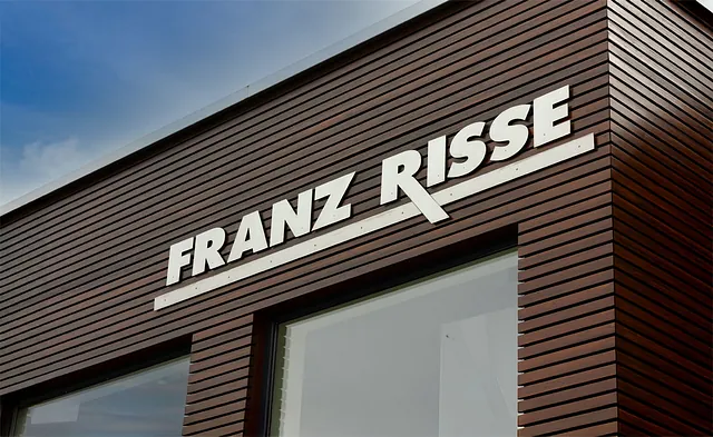 Fassadenansicht eines Gebäudes mit der Aufschrift 'FRANZ RISSE' in großen weißen Buchstaben auf einer Holzverkleidung