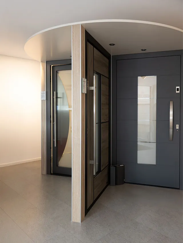 Moderner Eingangsbereich mit zwei nebeneinander stehenden Türen, eine aus Holz mit Glasfenster, die andere dunkelgrau mit vertikalem Glasfenster