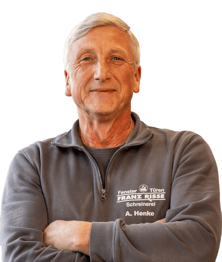 Mann mit grauem Pullover mit Reißverschluss und aufgedrucktem Text "Fenster Türen FRANZ RIESSE Schreinerei A. Henke" steht mit verschränkten Armen vor schwarzem Hintergrund
